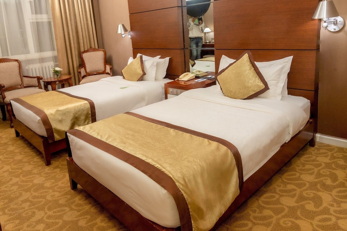 A hotel room with two beds, a desk, a chair, and a large mirror.