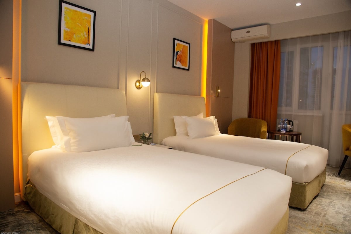 A hotel room with two beds, a small table with a chair, and artwork on the walls.