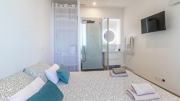 A modern hotel room with a bed, a shower area, a TV mounted on the wall, and a circular mirror. - T2 Town Center, Casino (Beausoleil)