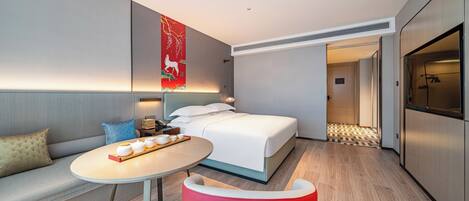 Una habitación de hotel moderna con una cama, una mesa redonda con teteras, una silla roja y una obra de arte grande en la pared.