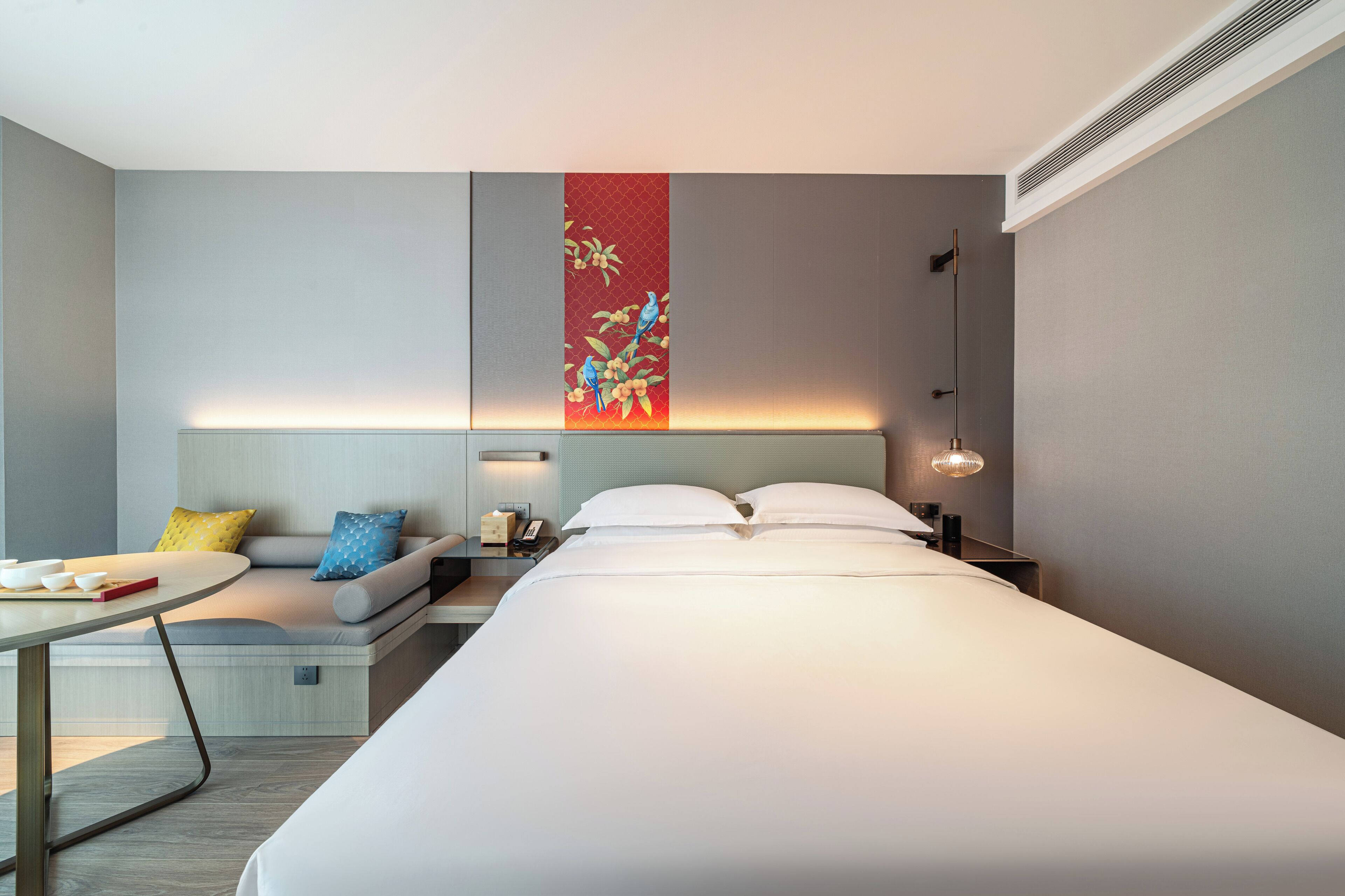 Una habitación de hotel moderna con una cama grande, una mesita de noche, un pequeño espacio para sentarse y una obra de arte colgada en la pared.