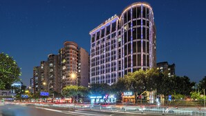 A multi-story hotel with illuminated signage, surrounded by other buildings and a busy street with visible traffic lights. - Echeng Hotel Guangzhou Baiyun Station (Guangzhou)