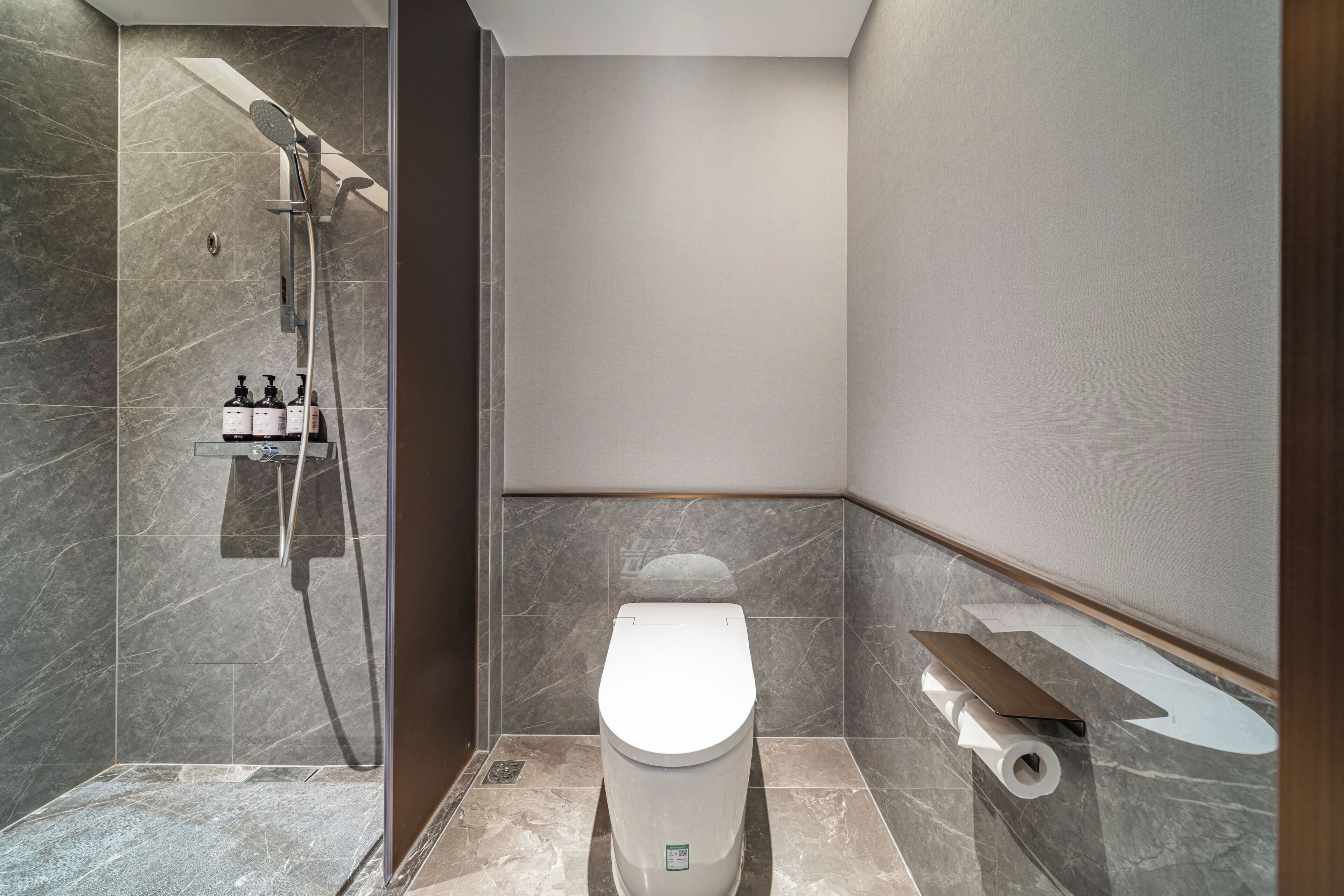 A modern bathroom with a shower, toilet, and a small shelf with toiletries.