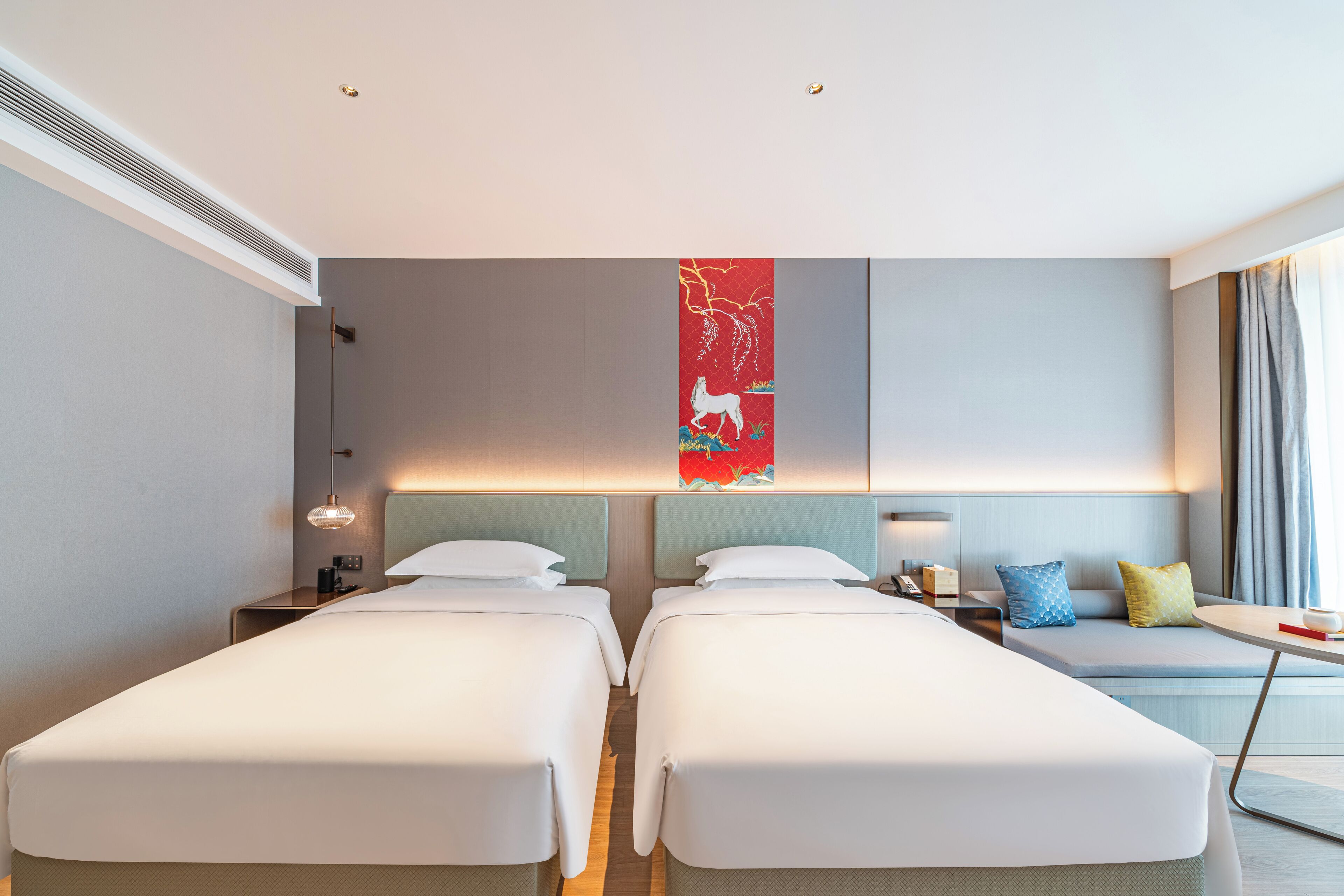 A hotel room with two beds, a sofa, a desk, and a large window with curtains.