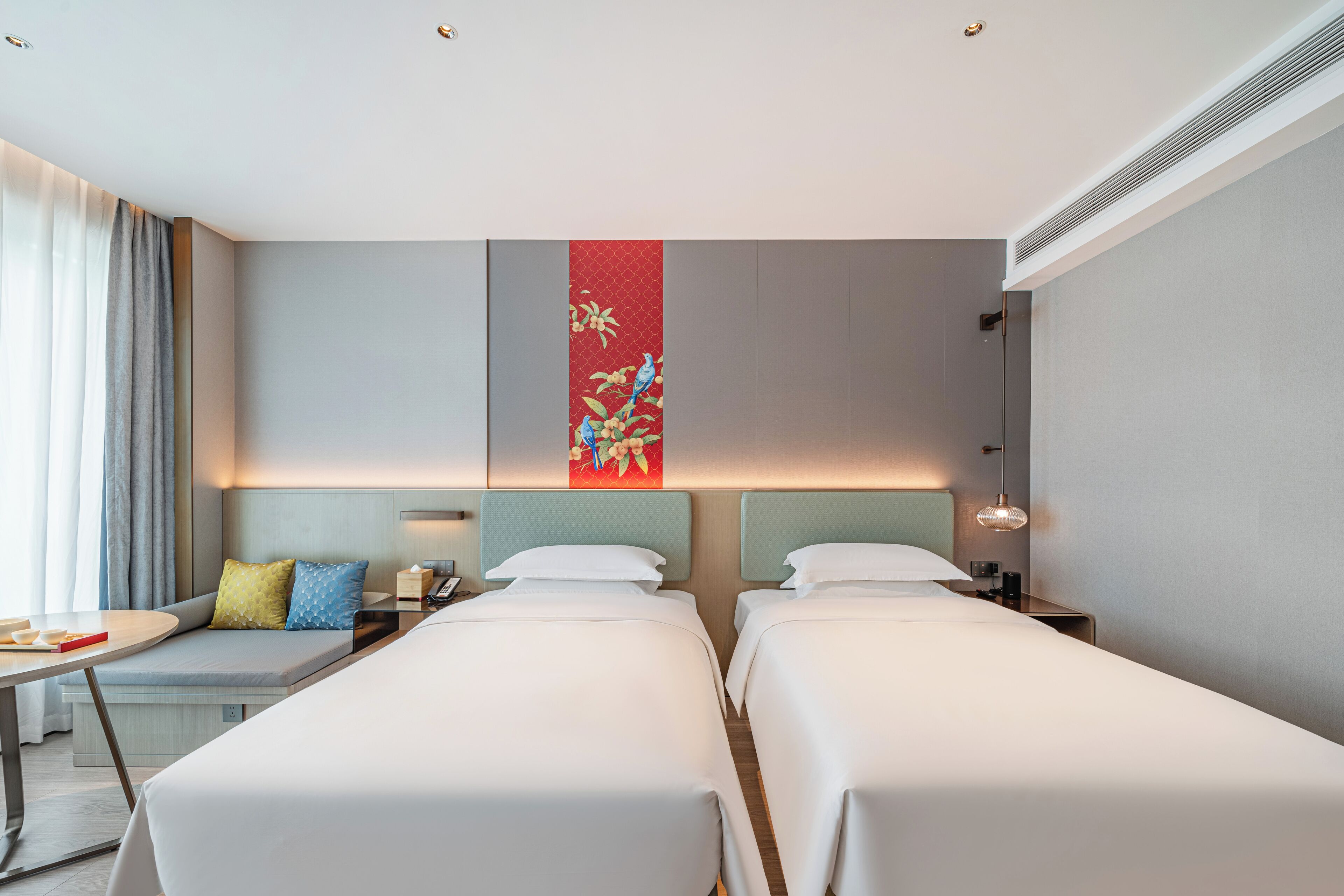 A hotel room with two beds, a small seating area, a desk, and a decorative wall panel.