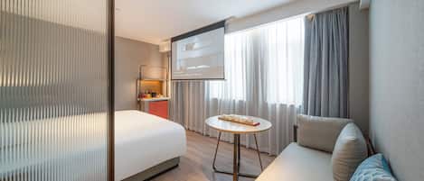 A hotel room with a bed, a sofa, a small table, a TV, and a window with curtains.