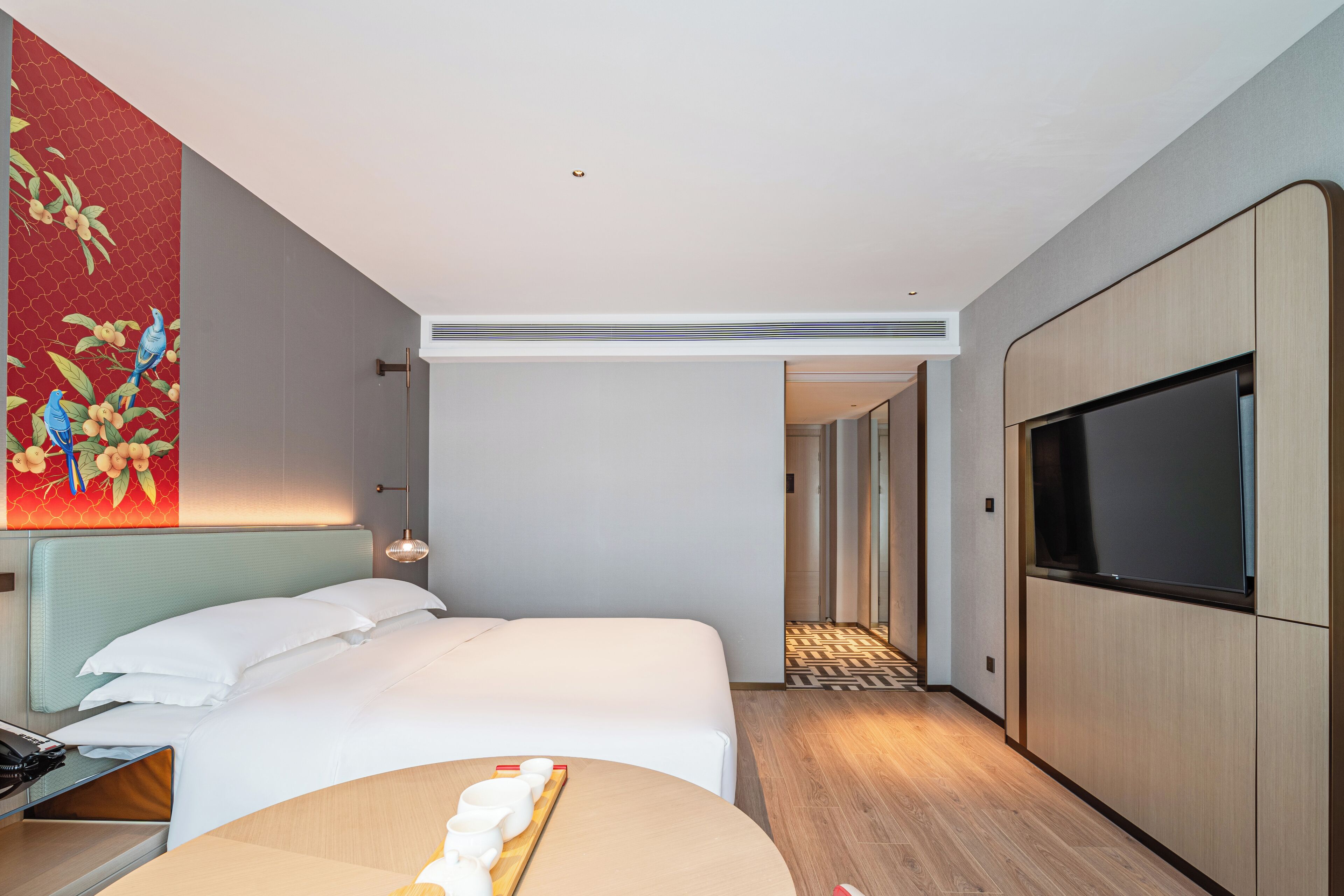 A modern hotel room with a bed, a TV, a wooden side table, and a large painting on the wall.
