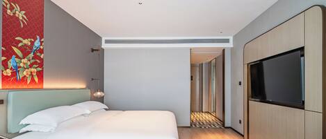 A modern hotel room with a bed, a TV, a wooden side table, and a large painting on the wall.