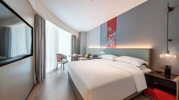 A modern hotel room with a large bed, a desk with a chair, a small table, and a red storage unit.