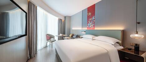 Une chambre d’hôtel moderne avec un grand lit, un bureau avec une chaise, une petite table et un meuble de rangement rouge.