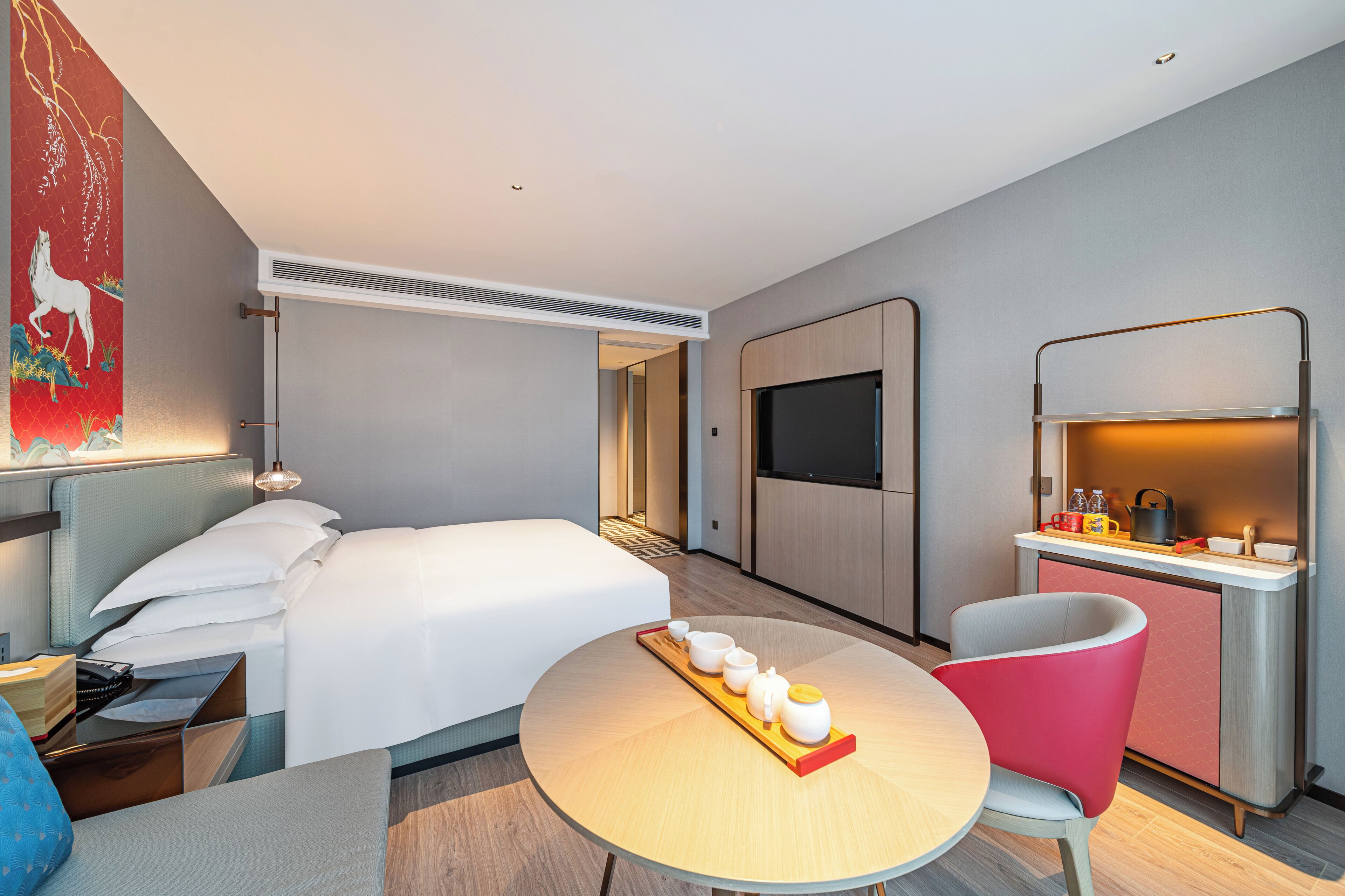 Et moderne hotelværelse med seng, spisebord med bakke med kopper, fjernsyn og tekøkken.