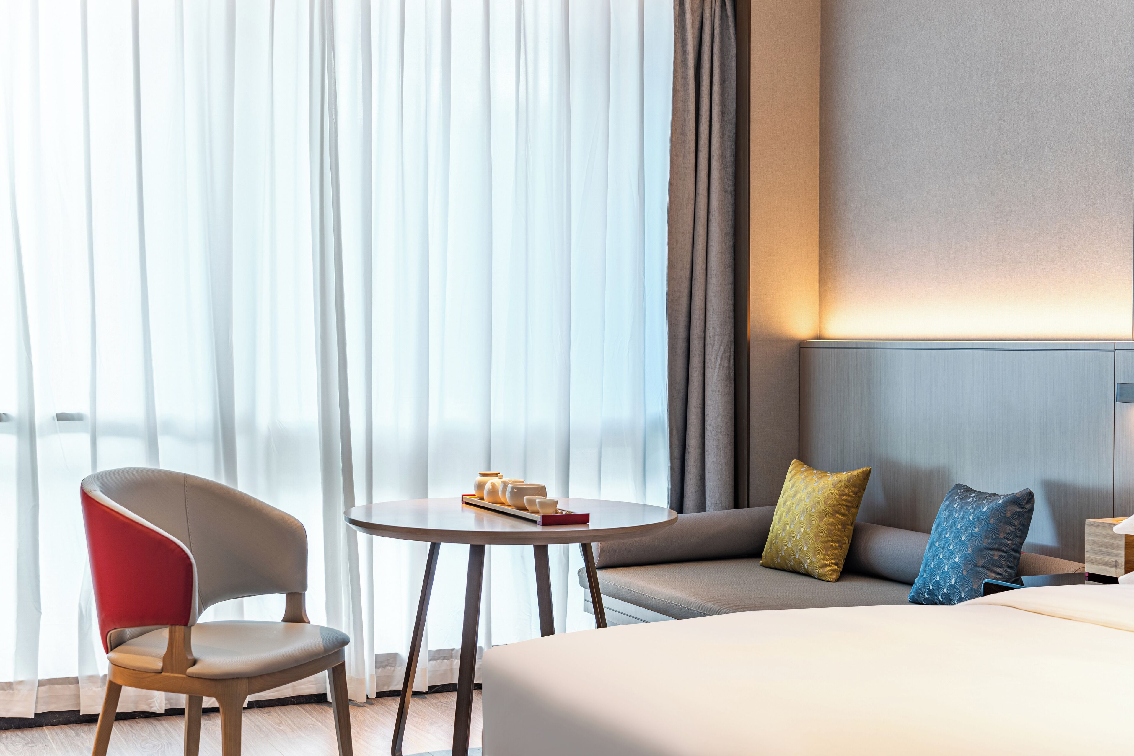 A hotel room with a bed, a sofa, a chair, and a small table with a book and a cup.