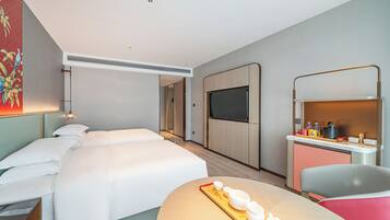 Ein modernes Hotelzimmer mit einem großen Bett, einem Schreibtisch mit Stuhl, einem Fernseher und einer kleinen Küchenzeile.