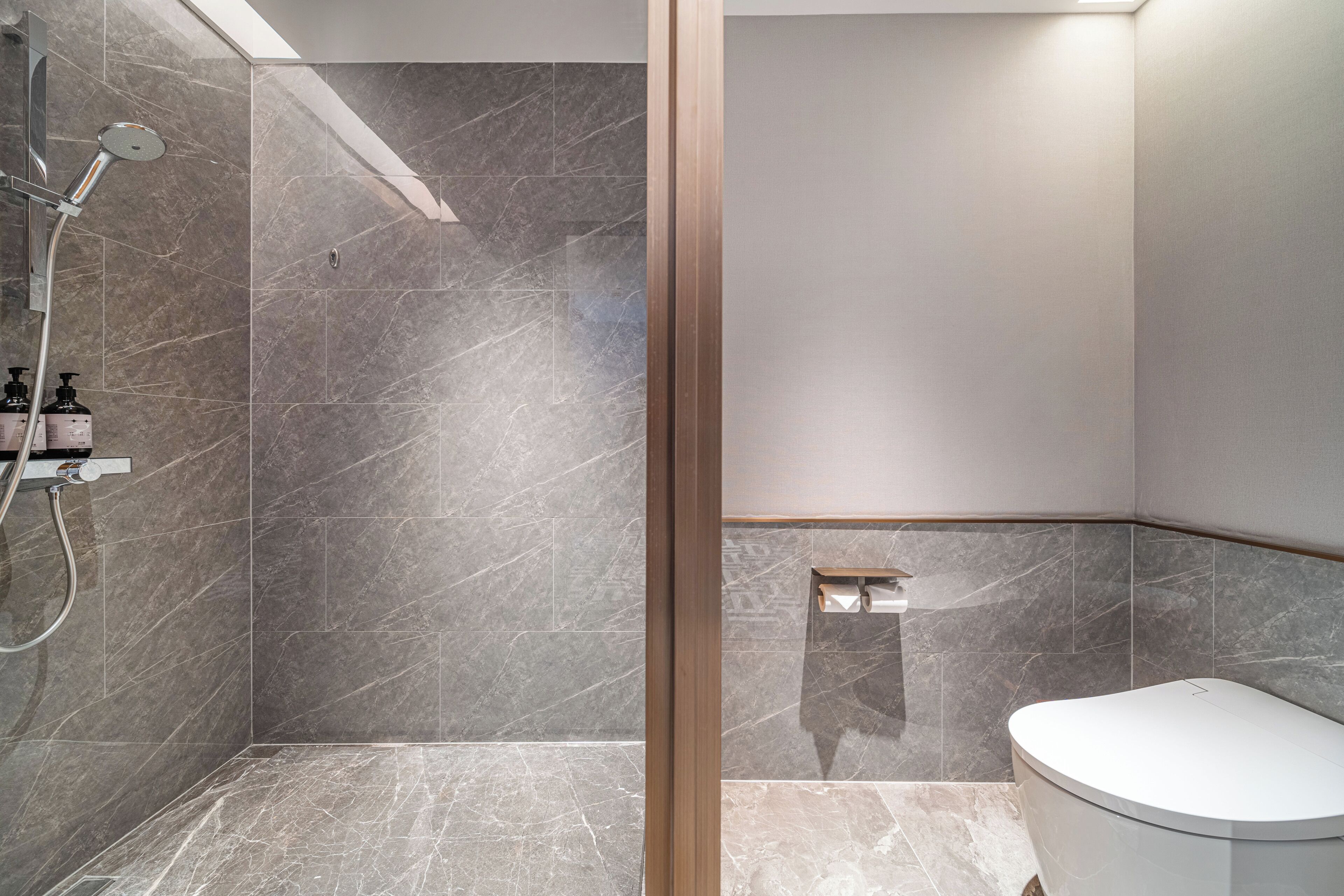 A modern bathroom with a shower, toilet, and marble tiles.