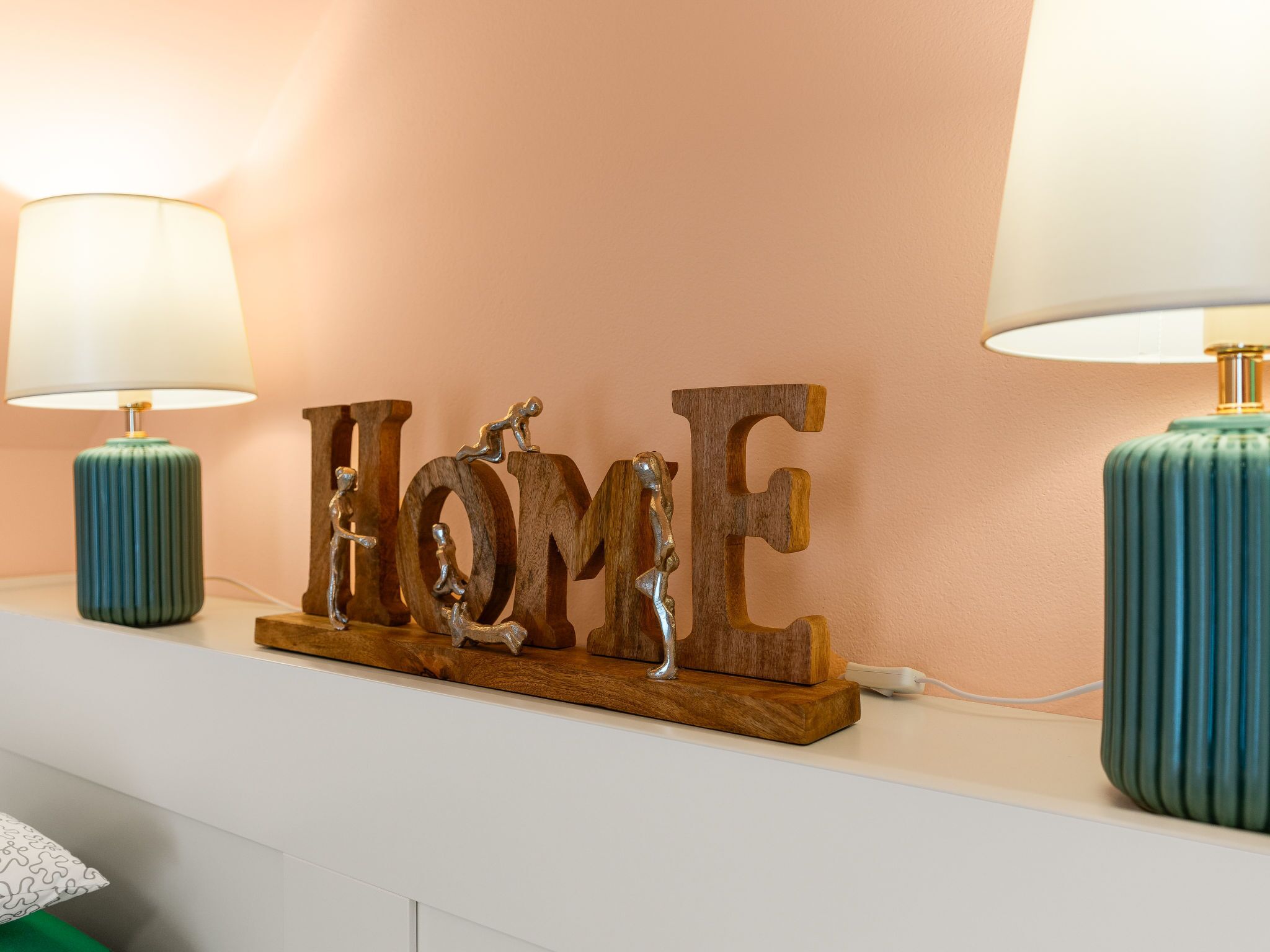Une décoration murale représentant le mot « HOME » et agrémentée de deux lampes, une de chaque côté.
