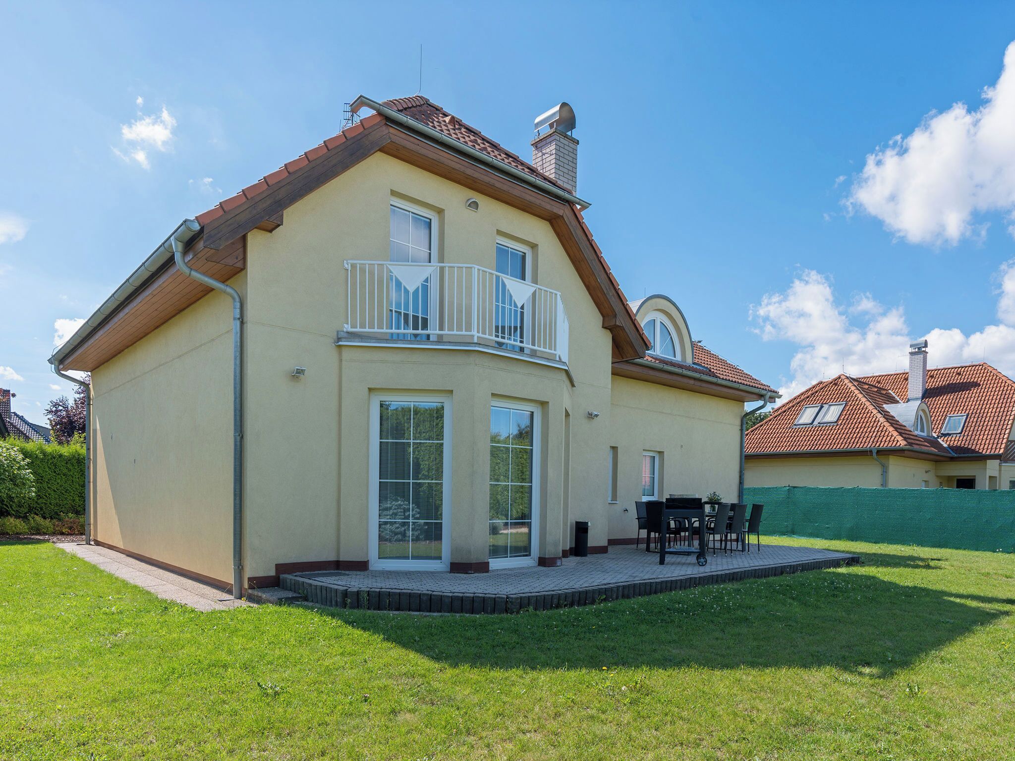 Une maison à deux étages dotée d’un balcon, d’une terrasse avec des meubles d’extérieur et d  ’une pelouse bien entretenue.