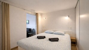 A hotel room with a bed, two pillows, a bedside table, a chair, and a door leading to another room. - T2, swimming pool, Tennis MC (Beausoleil)