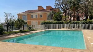 A rectangular swimming pool with a tiled deck, surrounded by a white fence and greenery. - T2, swimming pool, Tennis MC (Beausoleil)