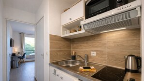A modern kitchen with a built-in microwave, stove, and sink. There is a small dining area with a table and chairs visible through an open door. - T2, swimming pool, Tennis MC (Beausoleil)