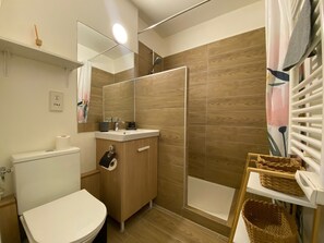 Un baño moderno con inodoro, lavamanos, espejo, ducha y una cesta en un estante.