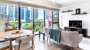 A modern living room with a large window, a dining area, and a TV.
