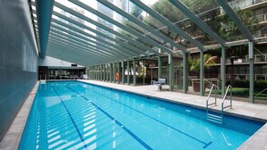 A swimming pool with clear blue water, surrounded by a covered area with glass walls and metal beams.