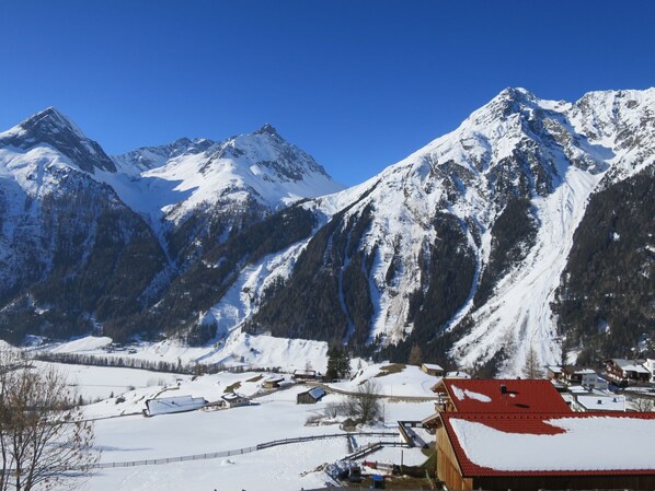 A mountain village with snow-covered peaks, a small settlement with buildings, and a clear blue sky.