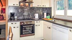 A modern kitchen with white cabinets, a stainless steel range hood, a built-in oven, a dishwasher, and a window with a view of trees. - Apart Jacqueline by Interhome (Huben)