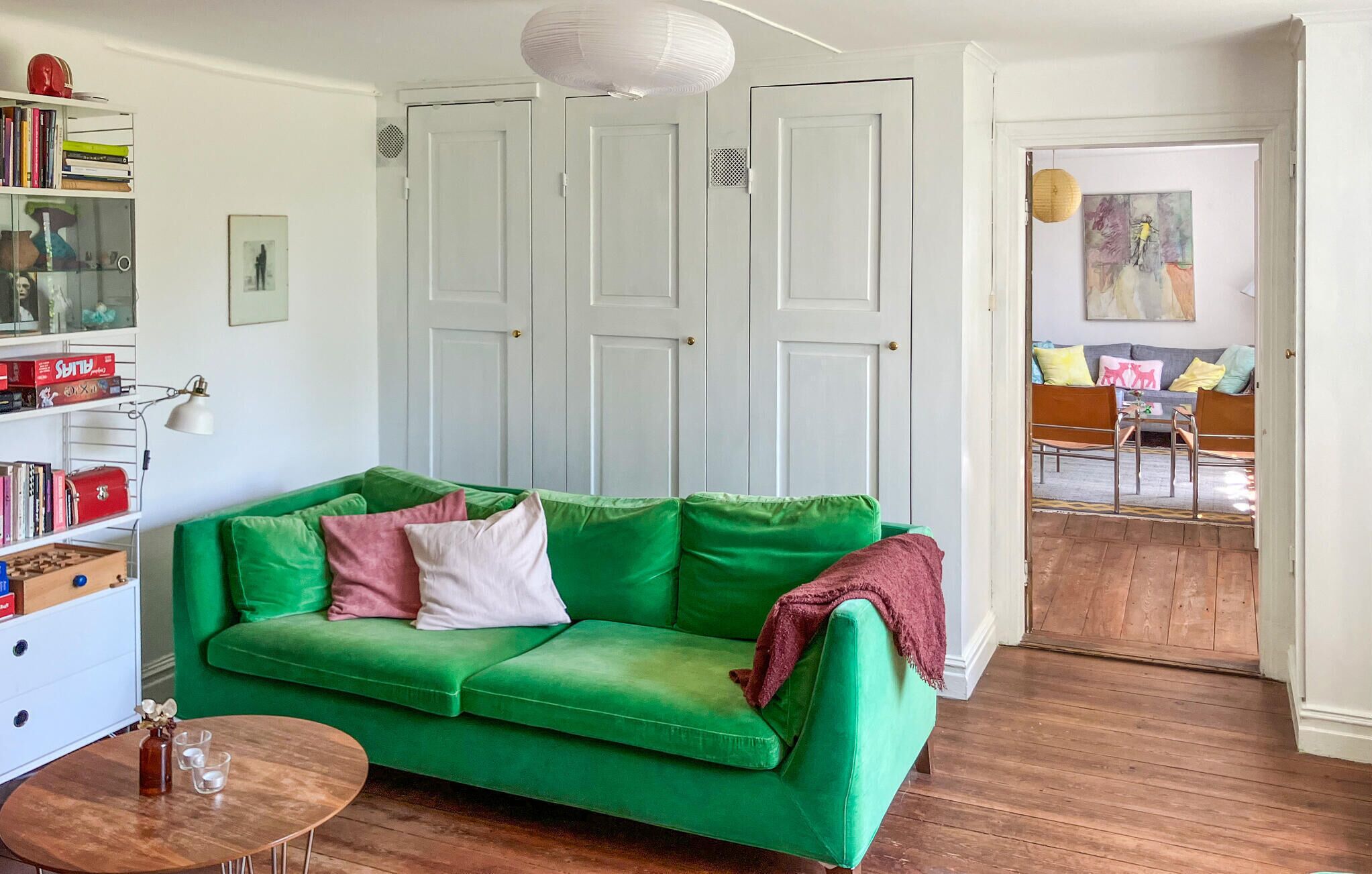 A green sofa in a room with white doors, a bookshelf, and a small table with glasses and a bottle.