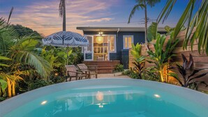 A pool area with a house in the background, surrounded by tropical plants and a sunset sky. - Barefoot Bay Cottage (Byron Bay)