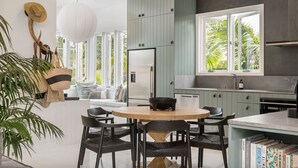 A modern kitchen with a round wooden table, dark chairs, and light green cabinets. - Barefoot Bay Cottage (Byron Bay)