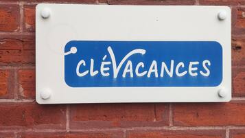 Ein Schild mit dem Text "CLÉVACANCES" vor weißem Hintergrund und blauer Umrandung, an einer Ziegelwand befestigt.