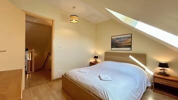 Een slaapkamer met een bed, bedlampen, een ingelijst beeld aan de muur en een dakraam.