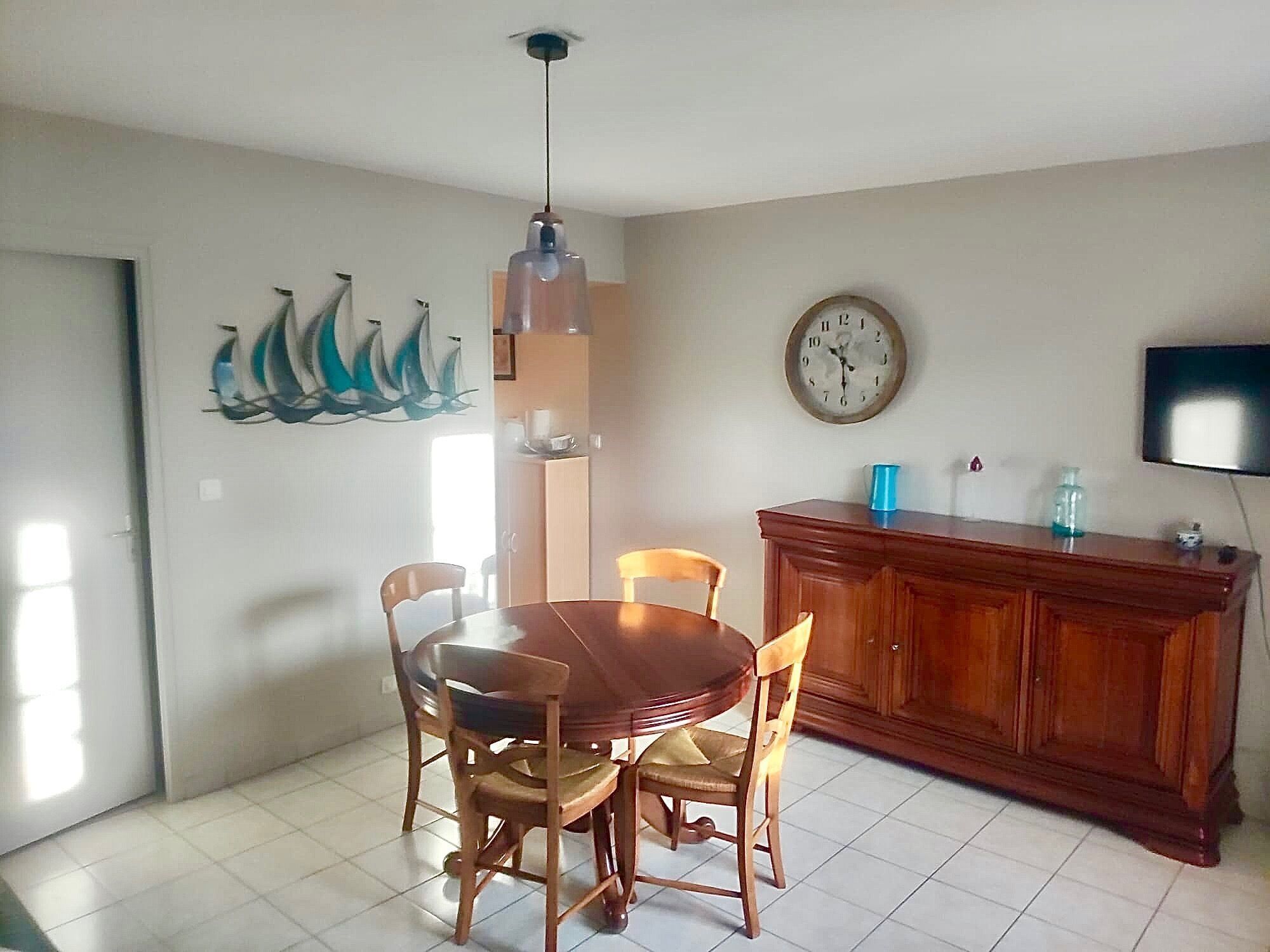 A dining area with a wooden table and chairs, a wall clock, a television, and a cabinet.