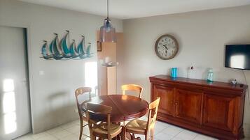 A dining area with a wooden table and chairs, a wall clock, a television, and a cabinet.