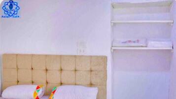 A bedroom with a tufted headboard, two pillows with colorful patterns, and a white shelf unit.