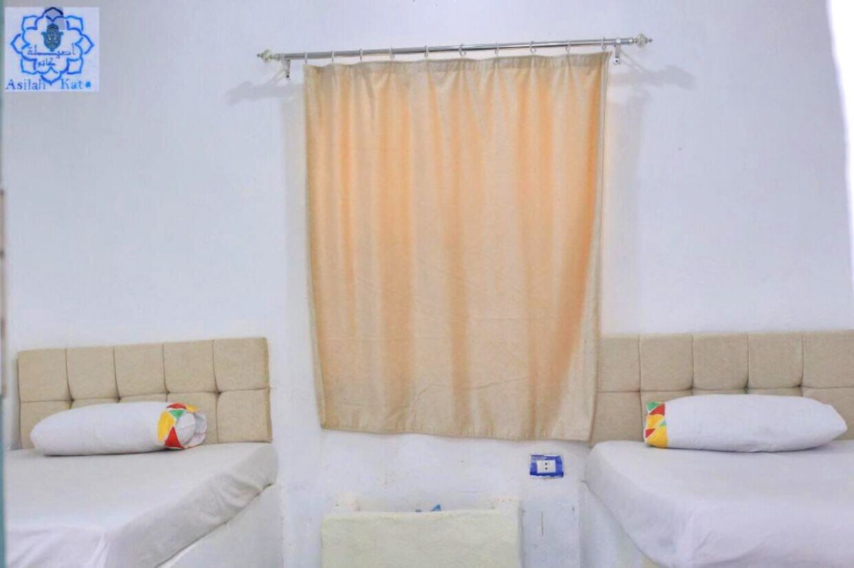 Una habitación con dos camas, cabeceros color beige y una cortina.