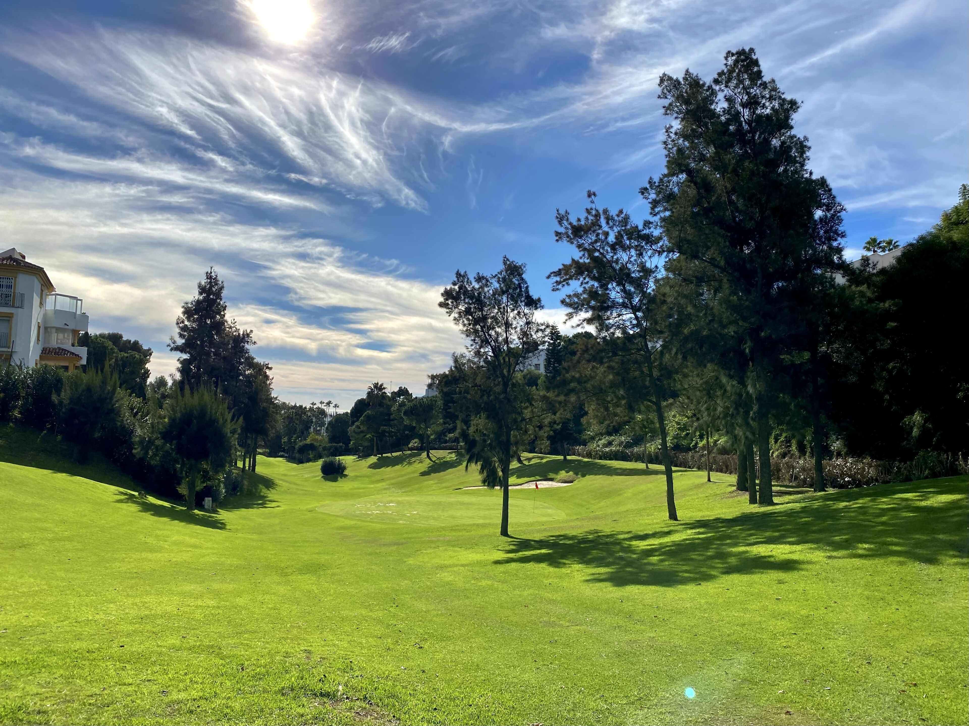 Een golfbaan met heldere lucht, bomen en een gebouw op de achtergrond.
