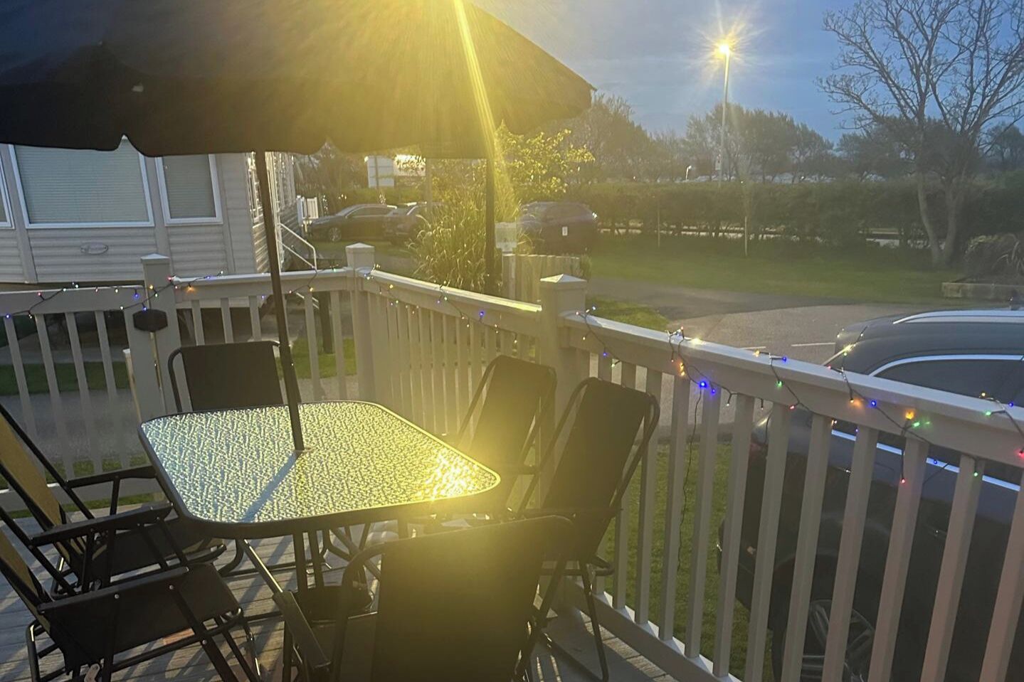 A covered outdoor patio with a table and chairs, surrounded by a white railing and string lights.