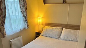 Quarto de hotel com cama, luminária de cabeceira, radiador e cortinas.