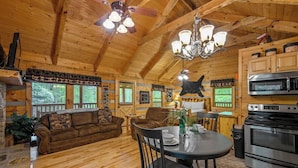 Interior de una cabaña de madera con comedor, cocina y ventilador de techo.