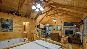 Interior de una cabaña de troncos con dormitorio, sala de estar, cocina y chimenea.