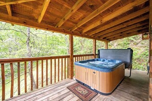 Une terrasse en bois avec un jacuzzi, des rampes en bois et une vue sur la forêt.