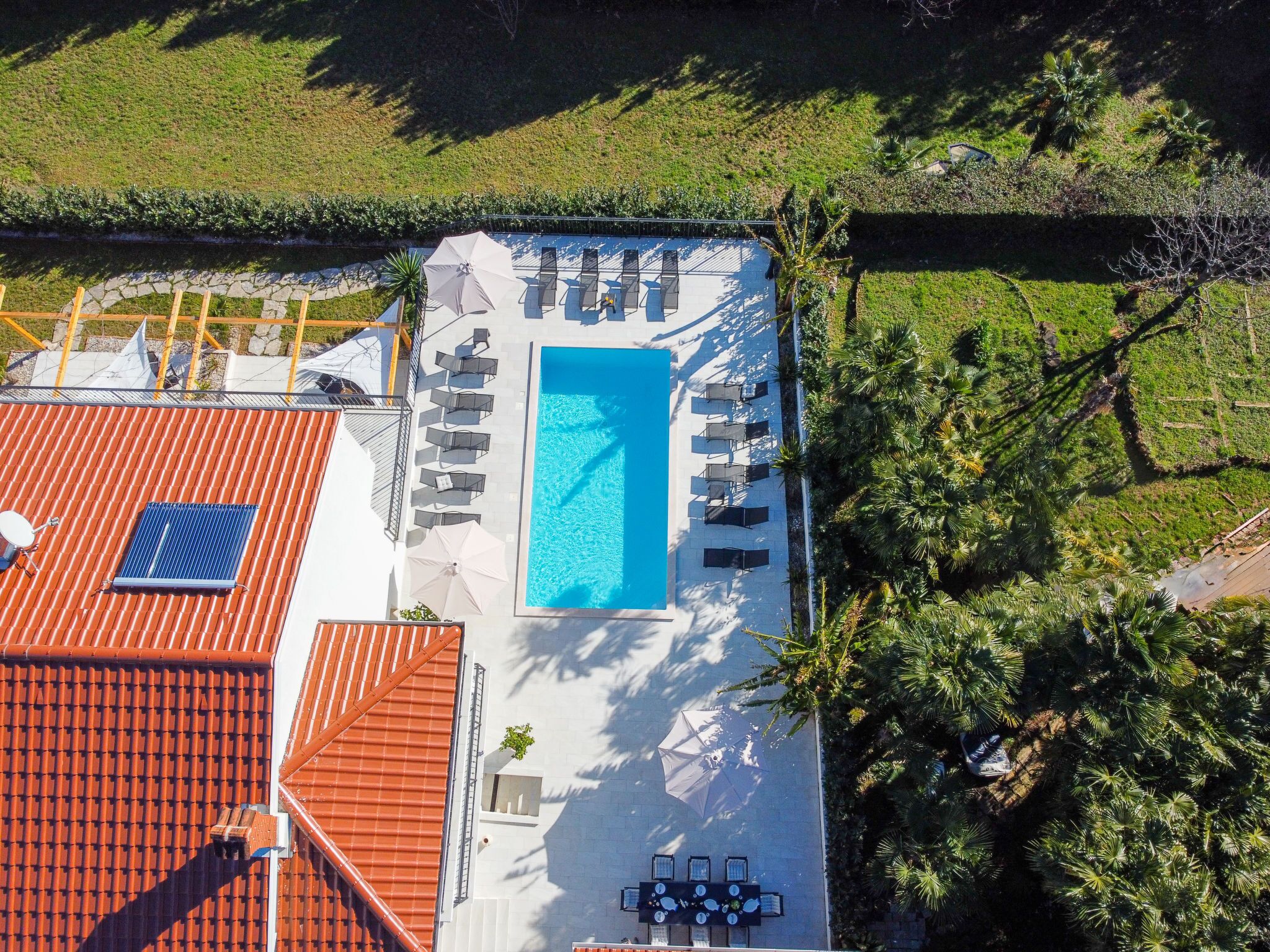 An aerial view of a rooftop with a swimming pool, sun loungers, and a red-tiled roof.