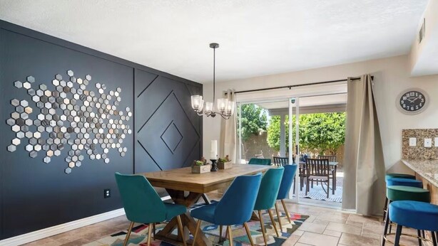 Un comedor con una mesa de madera y sillas azules, una pared decorativa con espejos hexagonales y vistas al exterior a través de un ventanal.