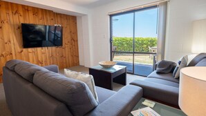 A modern living room with a grey sofa, a small table with a bowl, and a TV mounted on a wooden wall. - Etosha Villa @ Blue Seas (Scamander)