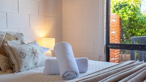 A neatly made bed with rolled white towels, a patterned pillow, and a bedside lamp. - Etosha Villa @ Blue Seas (Scamander)