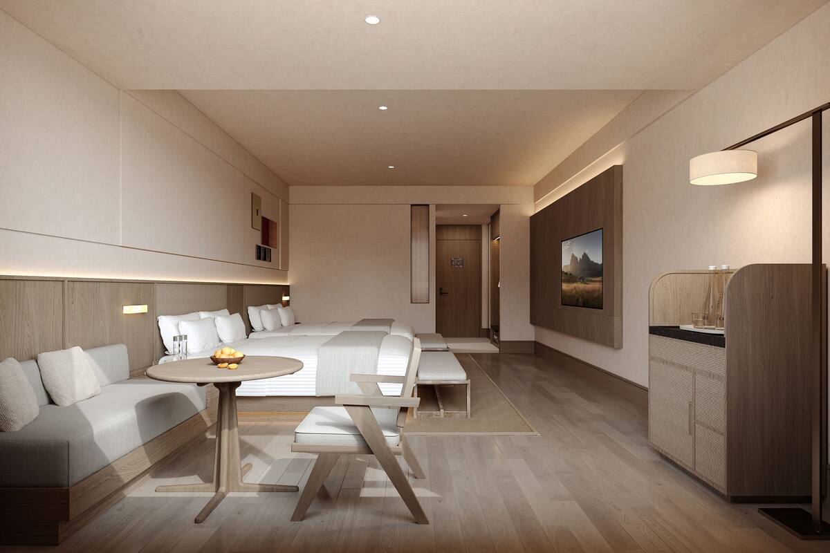 Una habitación de hotel moderna con un sofá, una mesita y una cama. Se observa un armario de madera y un televisor fijado a la pared.