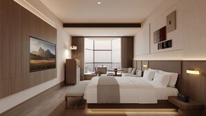Habitación de hotel moderna con una cama grande, vistas a la ciudad, un televisor montado y una pequeña mesa con una silla.
