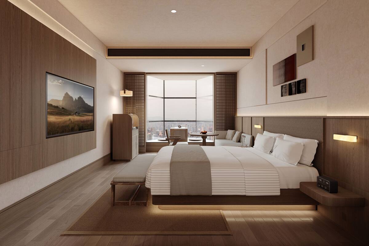 Habitación de hotel moderna con una cama grande, vistas a la ciudad, un televisor montado y una pequeña mesa con una silla.